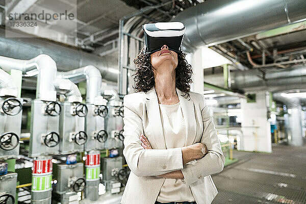 Geschäftsfrau mit verschränkten Armen und Virtual-Reality-Headset im Kraftwerk