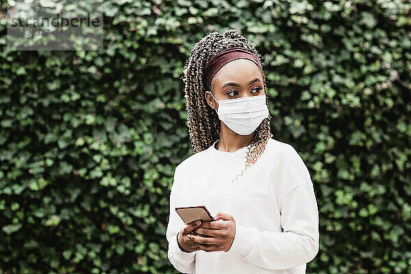 Junge Frau mit Gesichtsschutzmaske und Smartphone in der Hand