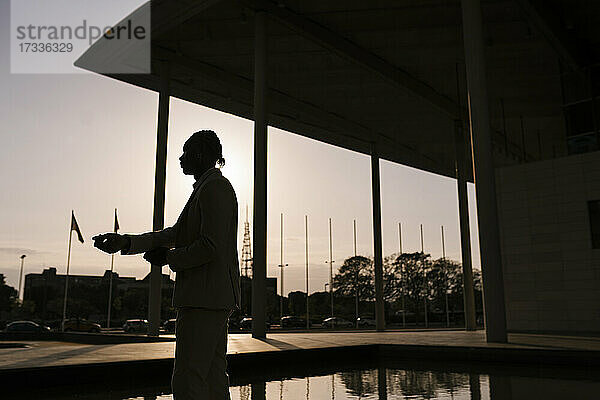 Silhouette junger Mann  der bei Sonnenuntergang an einem Gebäude steht