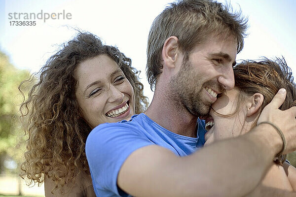 Glückliche lockig behaarte Frau schaut auf ein sich umarmendes Paar im Park