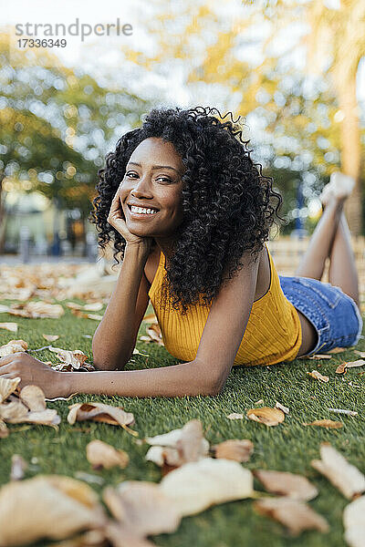 Glückliche junge Frau mit lockigem Haar im Gras liegend im Park