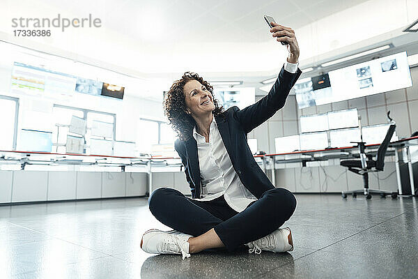 Lächelnde Geschäftsfrau  die ein Selfie mit ihrem Mobiltelefon am Hauptsitz macht