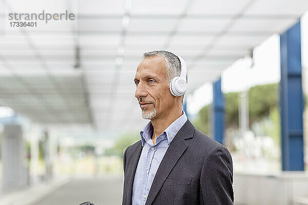 Geschäftsmann hört Musik über drahtlose Kopfhörer am Bahnhof