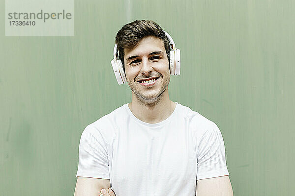 Lächelnder gut aussehender Mann mit Kopfhörern vor einer Wand
