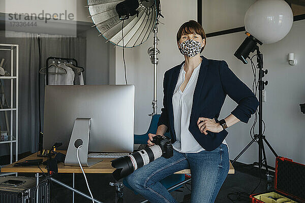 Fotografin mit Kamera auf dem Schreibtisch im Studio während einer Pandemie