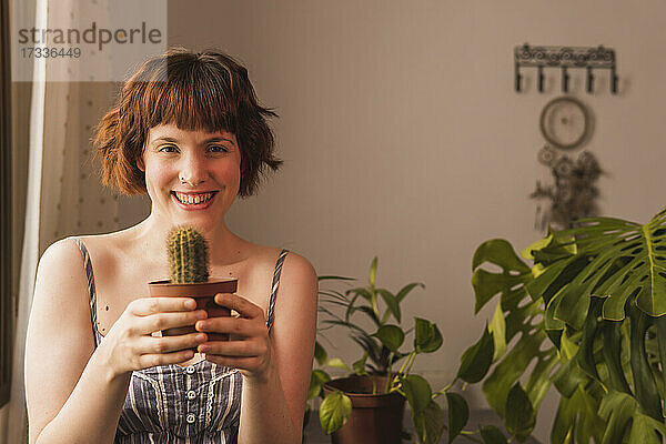 Glückliche Frau mit braunem Haar hält Kaktuspflanze zu Hause