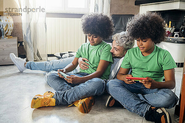 Junger Mann mit Zwillingsbrüdern benutzt sein Smartphone  während er zu Hause sitzt