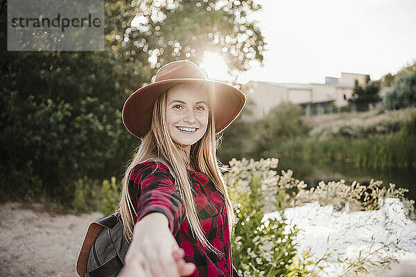 Glückliche schöne Frau mit Hut  die bei Sonnenuntergang die Hand eines Freundes hält