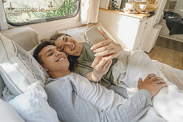 Glückliche Frau  die ein Selfie mit ihrem Freund macht  während sie auf dem Bett im Wohnmobil liegt