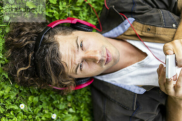 Junger gut aussehender Mann hört Musik über Kopfhörer im Gras liegend