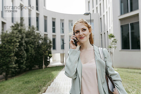 Weibliche Fachkraft  die wegschaut  während sie im Büropark mit einem Mobiltelefon spricht