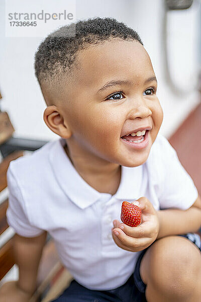 Lächelnder Junge schaut weg und hält eine Erdbeere