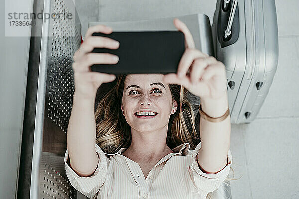 Glückliche junge Frau  die am Bahnhof liegend ein Video auf ihrem Mobiltelefon anschaut