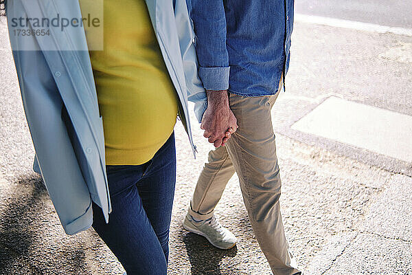 Schwangere Frau hält die Hand ihres Mannes beim Gehen auf der Straße