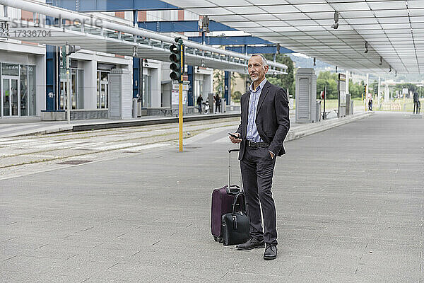 Geschäftsmann mit Gepäck wartet auf Zug am Bahnhof