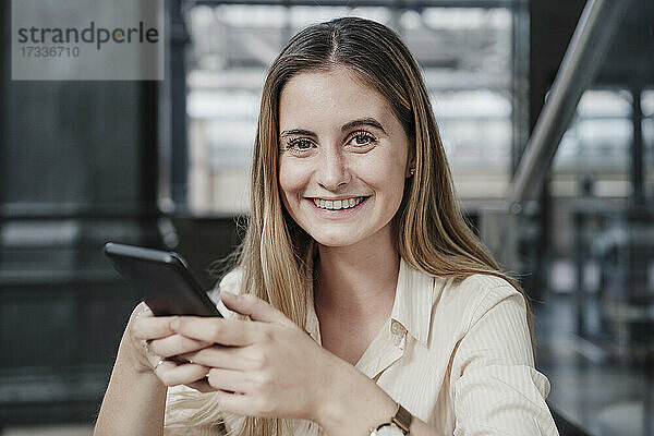 Lächelnde junge schöne Frau sitzt mit Handy im Café
