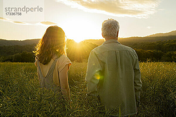 Vater und Tochter stehen bei Sonnenuntergang auf einem Feld