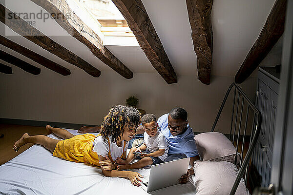 Vater und Mutter mit Sohn benutzen Laptop auf dem Dachboden zu Hause
