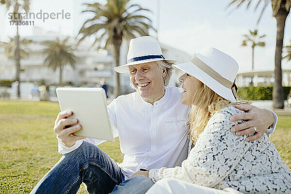 Glückliches reifes Paar mit Hüten bei einem Videoanruf über ein digitales Tablet im Urlaub