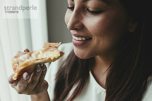Lächelnde Frau isst ein Stück Pizza zu Hause