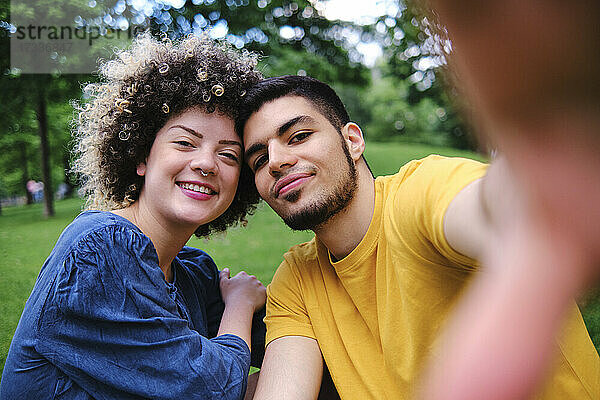 Lächelnde  lockig behaarte Frau sitzt mit ihrem Freund im Park