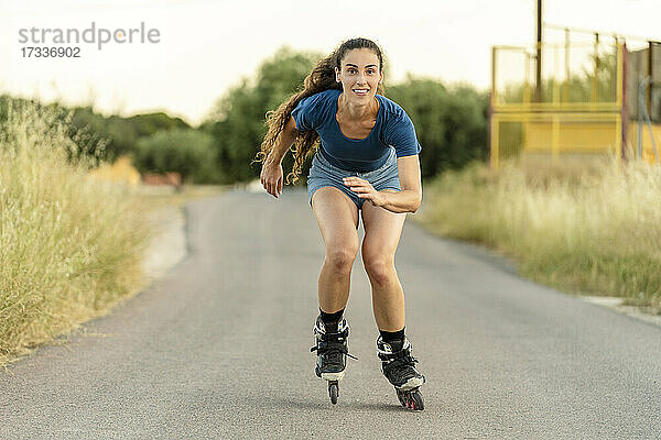 Lächelnde junge Frau beim Rollschuhlaufen auf der Straße