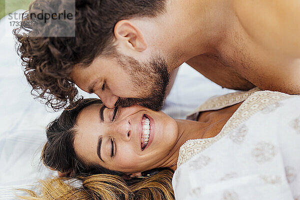 Zärtlicher Mann küsst glückliche Freundin mit geschlossenen Augen auf Decke liegend