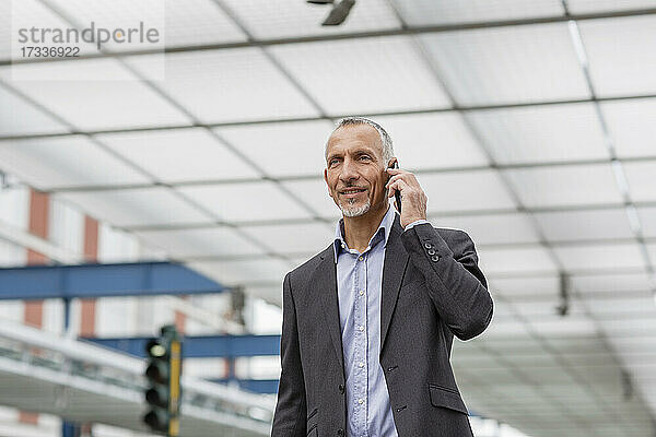 Geschäftsmann spricht am Bahnhof mit seinem Smartphone