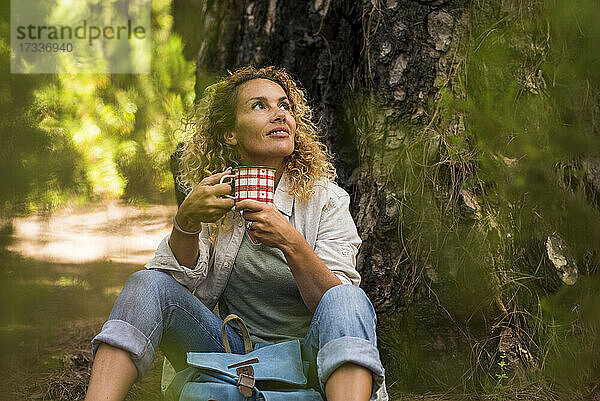 Frau schaut weg  während sie eine Kaffeetasse im Wald hält