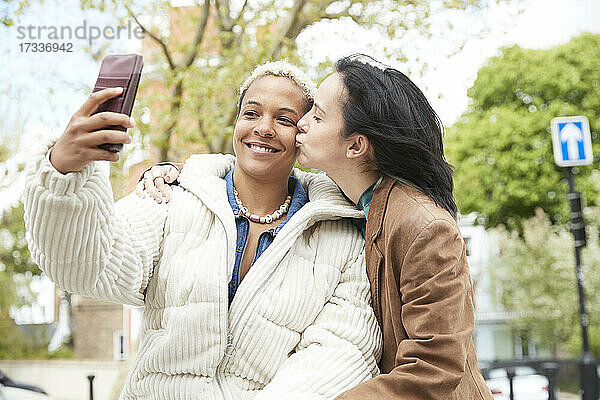 Lächelnde Frau nimmt Selfie mit Freundin küssen auf Wange