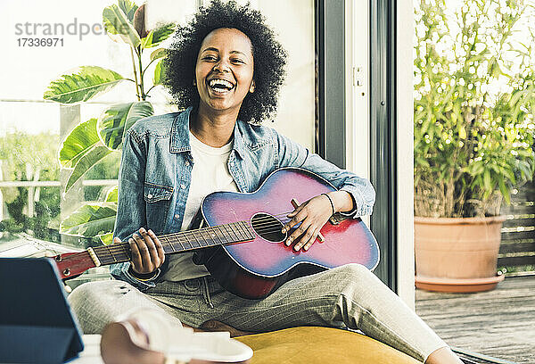 Fröhliche Frau spielt Gitarre  während sie zu Hause sitzt