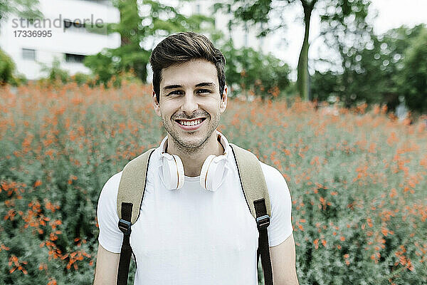Lächelnder junger Mann  der einen Rucksack trägt  während er vor einer Wiese steht