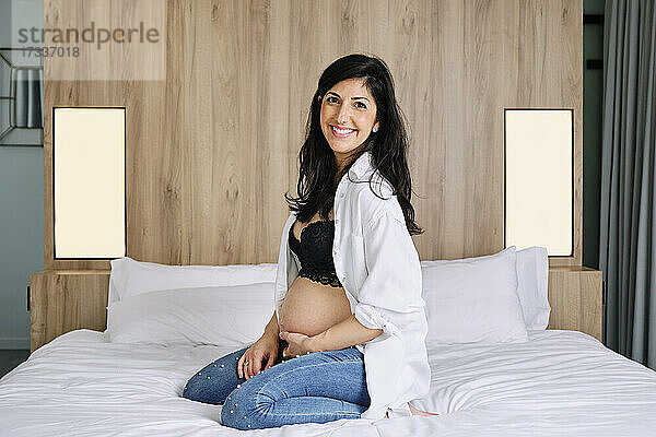 Glückliche schwangere Frau sitzt zu Hause im Bett