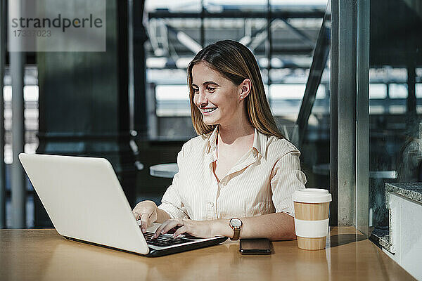 Lächelnde junge Geschäftsfrau mit Laptop am Tisch in einem Cafe