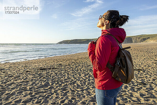 Frau mit Rucksack genießt die Einsamkeit am Strand bei Sonnenuntergang