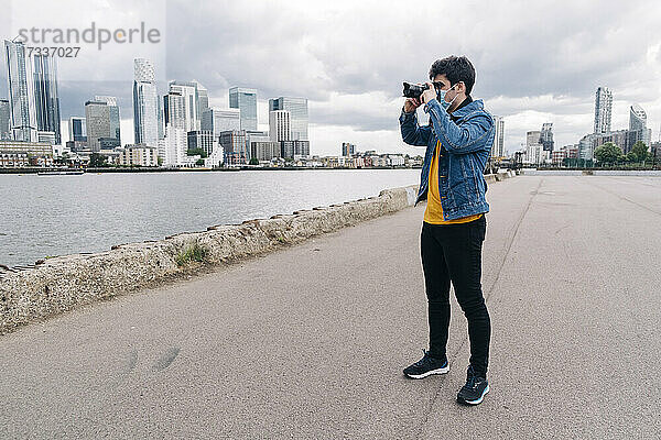 Junger Mann fotografiert durch die Kamera  während er auf der Promenade steht  während der Pandemie