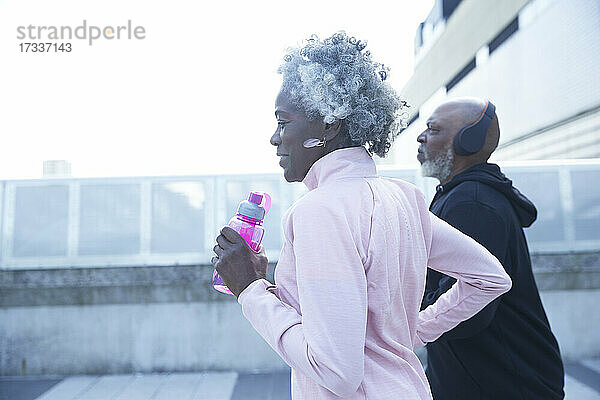 Ältere Frau hält Wasserflasche beim Laufen mit reifem Mann