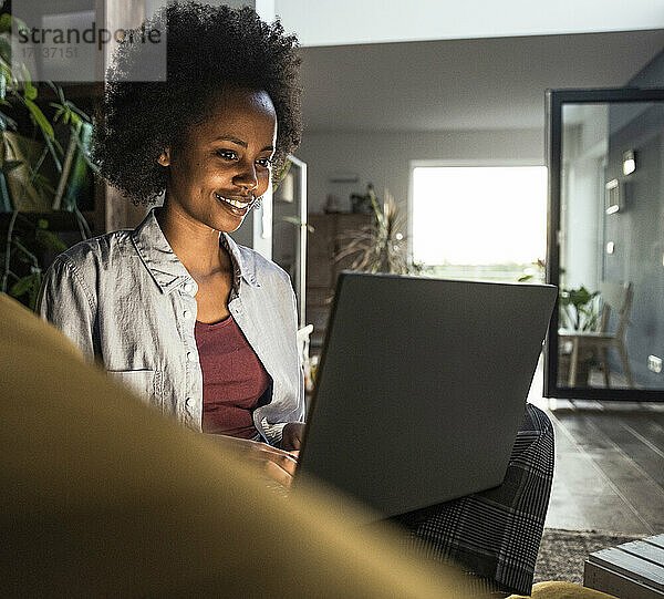 Lächelnde Geschäftsfrau  die einen Laptop benutzt  während sie zu Hause sitzt