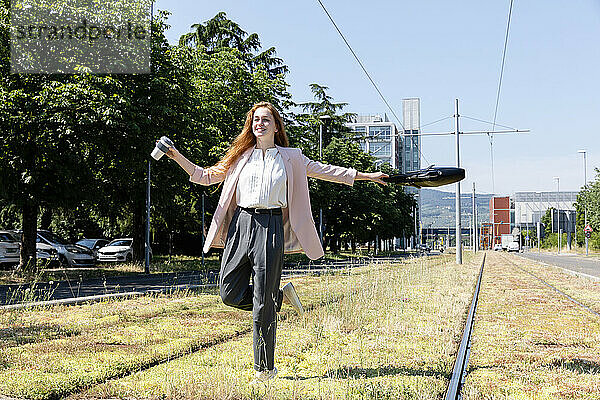Lächelnde weibliche Fachkraft  die wegschaut  während sie eine Tasche inmitten von Eisenbahnschienen schwingt