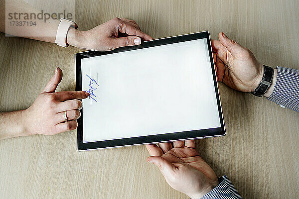 Geschäftsfrau  die eine Unterschrift leistet  während ein Geschäftsmann ein digitales Tablet am Schreibtisch im Büro hält