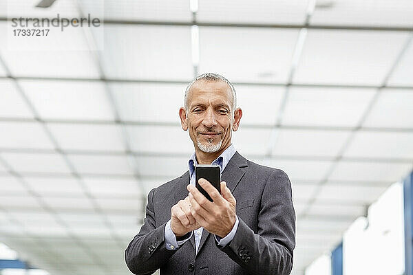 Lächelnder Geschäftsmann mit Smartphone am Bahnhof