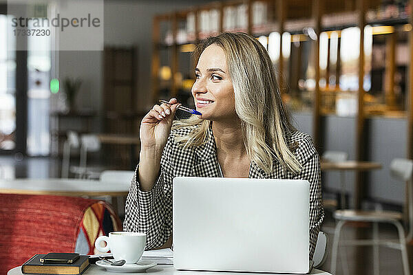 Lächelnde weibliche Fachkraft  die mit einem Laptop in einem Café sitzt und wegschaut