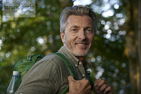 Lächelnder männlicher Wanderer mit Rucksack im Wald