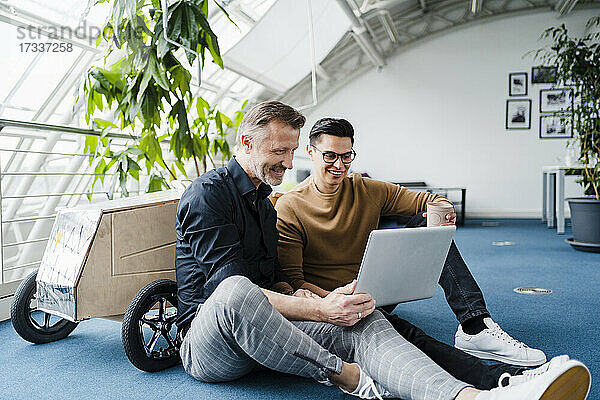 Männliche Kollegen  die einen Laptop benutzen  während sie im Kreativbüro sitzen