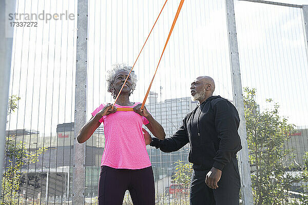 Mann hilft Frau beim Training mit Widerstandsbändern im Park an einem sonnigen Tag