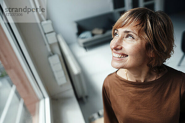 Geschäftsfrau lächelt  während sie am Fenster im Büro nach oben schaut