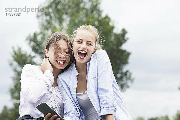 Freundinnen lachen  während sie ihr Smartphone in der Natur halten