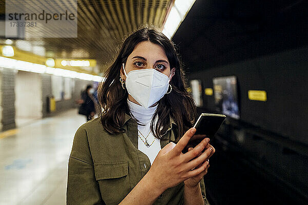 Frau mit Gesichtsmaske und Mobiltelefon in der U-Bahn stehend