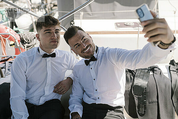Lächelnder Mann nimmt Selfie mit männlichem Freund durch Handy in Yacht