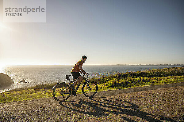 Älterer männlicher Sportler  der bei Sonnenuntergang auf der Straße Rad fährt